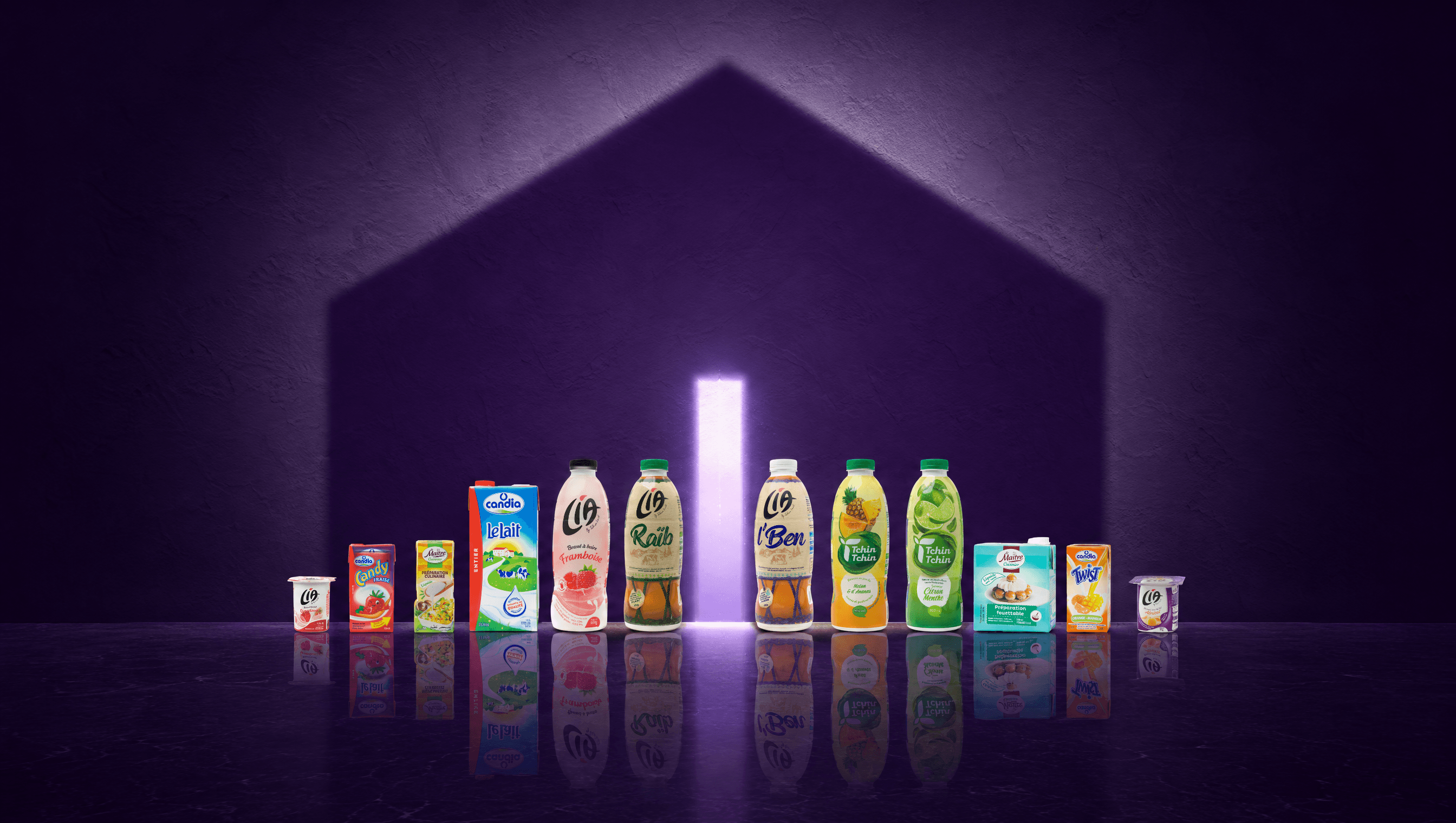 Douze emballages des marques du groupe alignés sur un sol brillant ; leur ombre dessine une maison sur un mur violet, avec une porte de lumière au centre.
